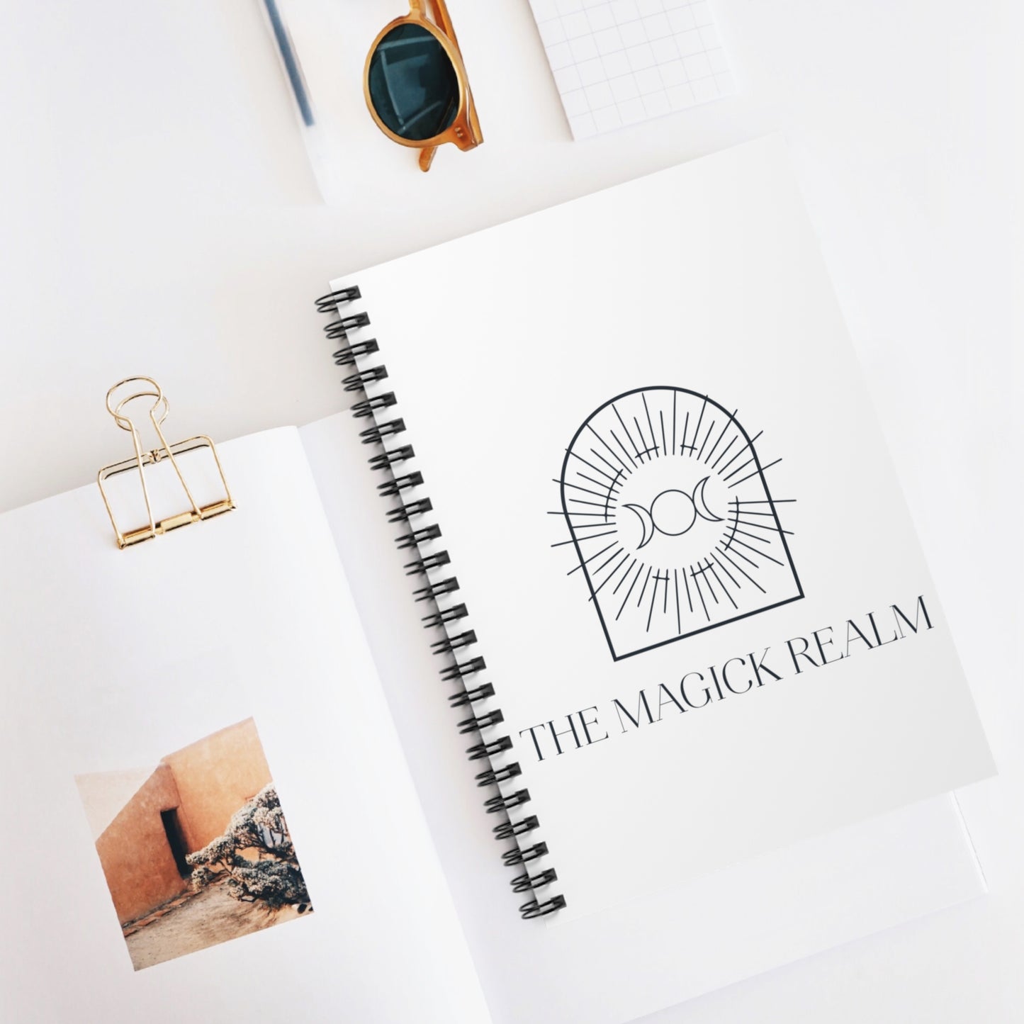 Notebook with 'The Magick Realm' logo on a white surface
