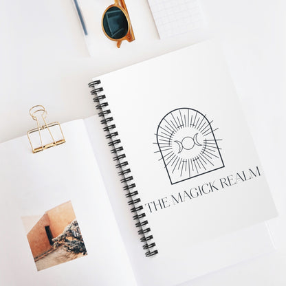 Notebook with 'The Magick Realm' logo on a white surface